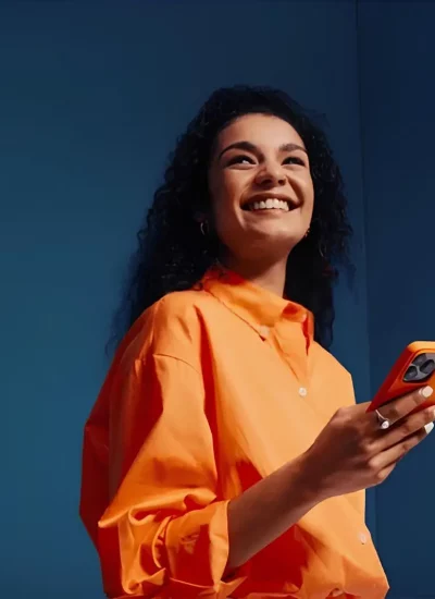 Personne en chemise orange utilisant un smartphone sur fond bleu uni